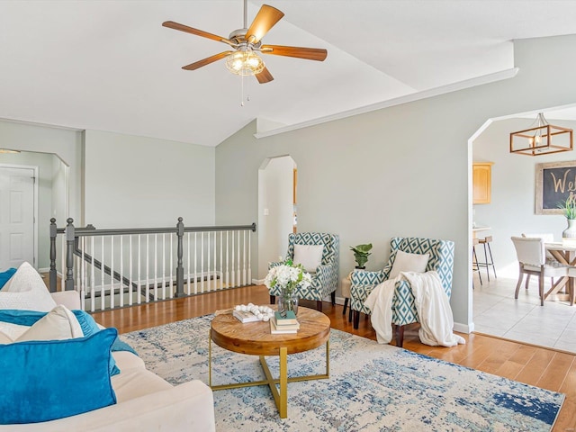 living area with wood finished floors, baseboards, lofted ceiling, arched walkways, and ceiling fan with notable chandelier