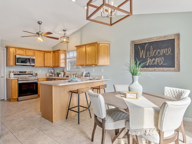 kitchen featuring light countertops, vaulted ceiling, a peninsula, light tile patterned flooring, and stainless steel appliances