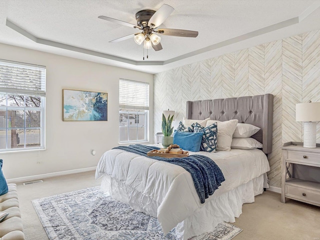 bedroom with visible vents, baseboards, a textured ceiling, a raised ceiling, and light colored carpet