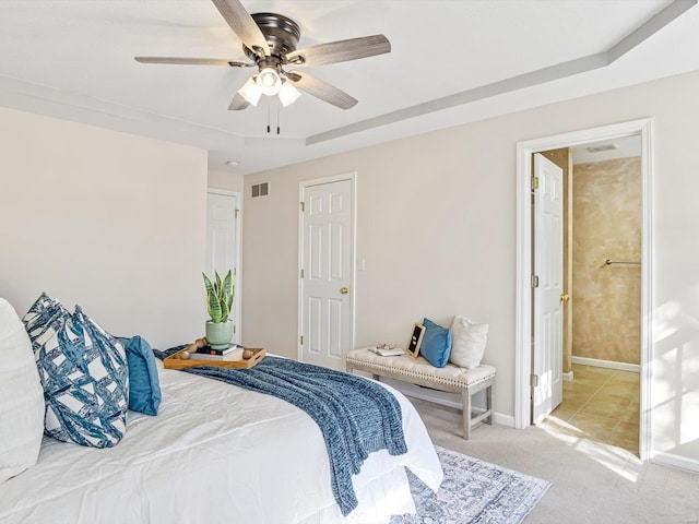 bedroom with visible vents, baseboards, a tray ceiling, light carpet, and a ceiling fan