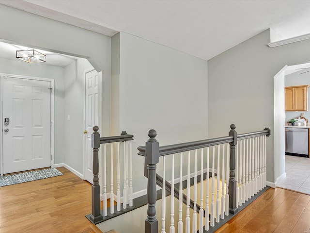 corridor featuring baseboards, an upstairs landing, light wood-style floors, and arched walkways