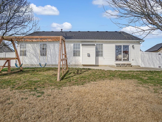 rear view of house with a patio, fence, roof with shingles, a yard, and a playground