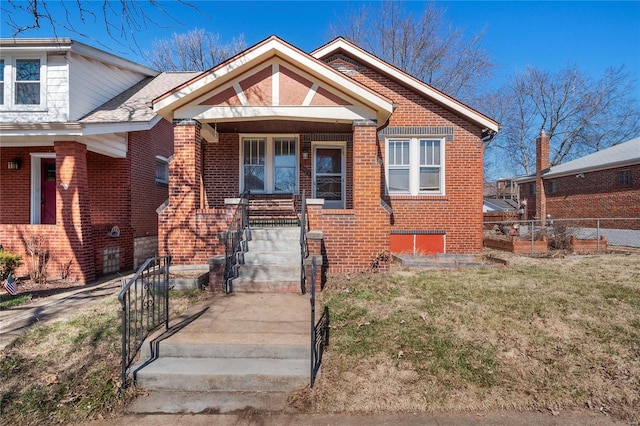 bungalow-style home featuring a front lawn, fence, and brick siding