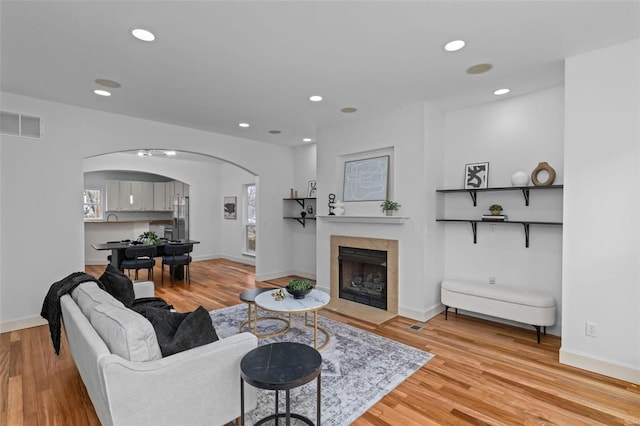 living room featuring a tiled fireplace, light wood-style flooring, recessed lighting, and visible vents