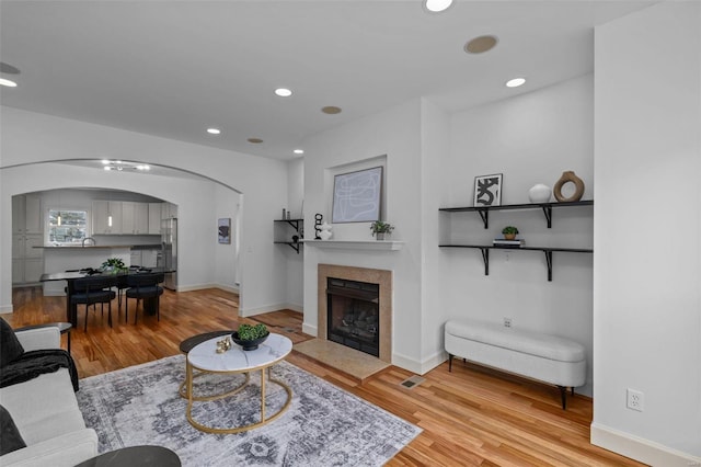 living room featuring a fireplace with flush hearth, recessed lighting, arched walkways, and light wood finished floors