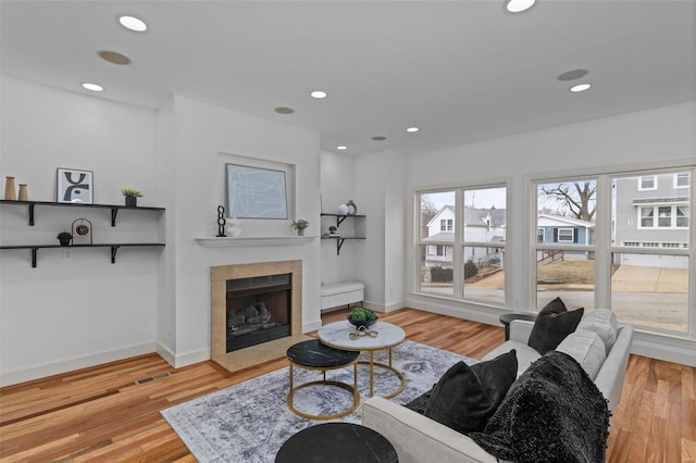 living area with recessed lighting, baseboards, a fireplace with flush hearth, and wood finished floors