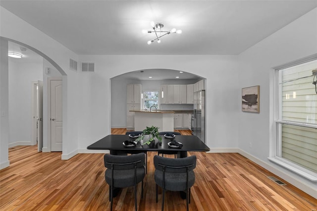 dining space with arched walkways, visible vents, and light wood-type flooring