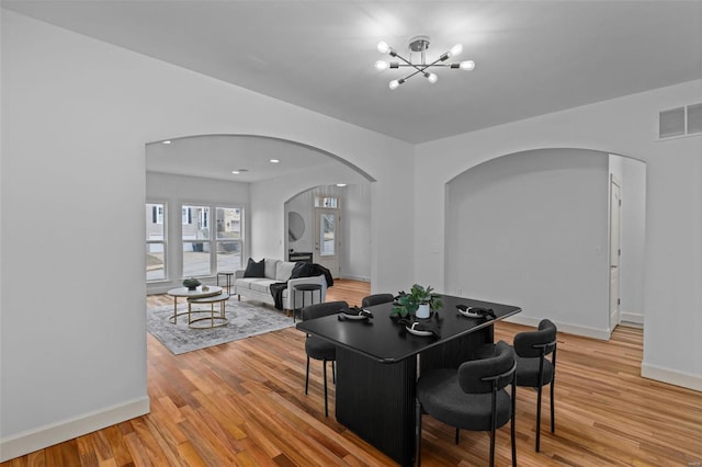 dining area featuring visible vents, baseboards, a chandelier, light wood-style flooring, and arched walkways