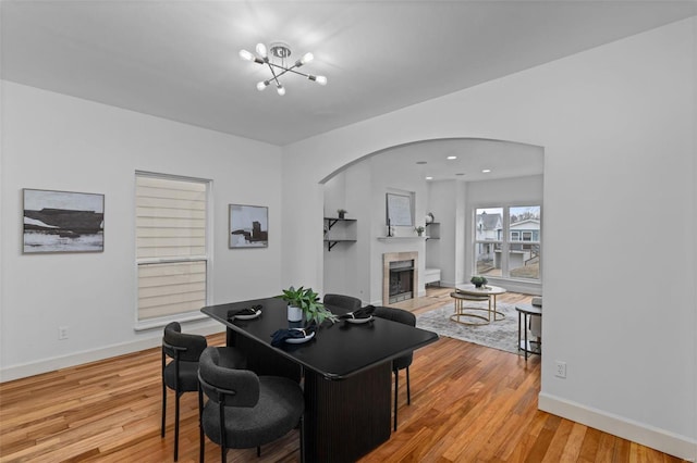 dining space featuring baseboards, a chandelier, a tile fireplace, light wood-style floors, and arched walkways