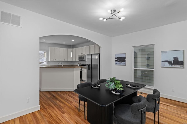 dining space with visible vents, arched walkways, baseboards, and light wood finished floors