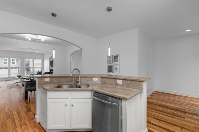 kitchen featuring arched walkways, a sink, open floor plan, dishwasher, and light wood-type flooring