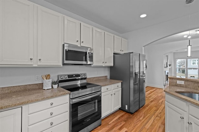 kitchen with white cabinetry, stainless steel appliances, arched walkways, light wood finished floors, and hanging light fixtures