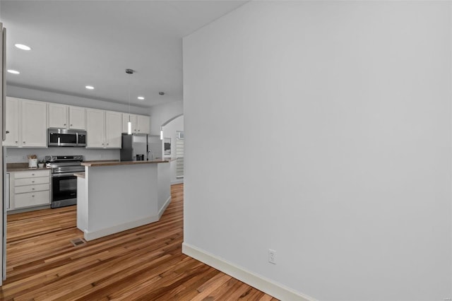 kitchen with light wood finished floors, recessed lighting, stainless steel appliances, arched walkways, and white cabinetry