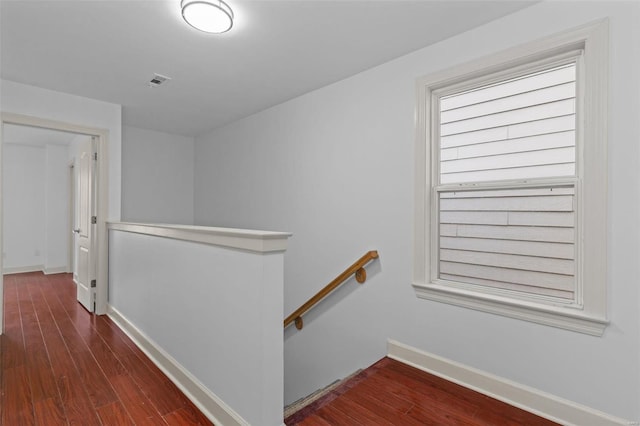 hall with dark wood finished floors, visible vents, an upstairs landing, and baseboards