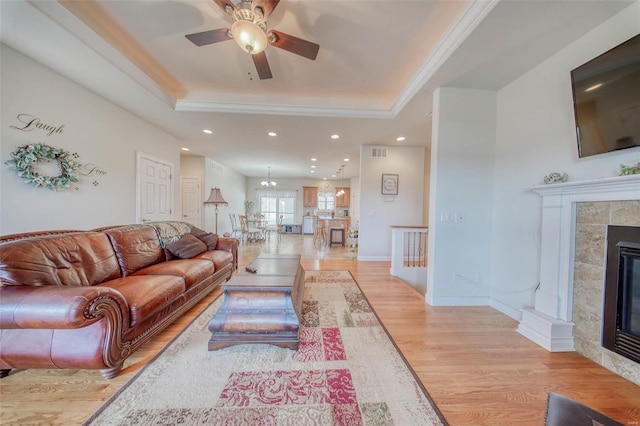 living area with visible vents, ceiling fan, light wood-style flooring, a fireplace, and a raised ceiling