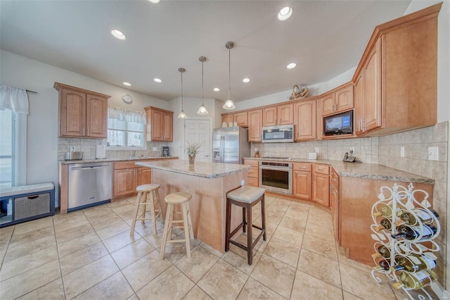 kitchen featuring a breakfast bar area, light stone counters, a sink, stainless steel appliances, and a center island