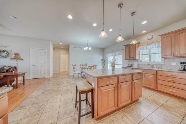 kitchen featuring visible vents, a notable chandelier, backsplash, a center island, and light stone countertops