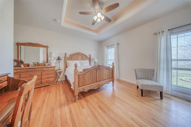 bedroom with light wood-type flooring, visible vents, baseboards, a raised ceiling, and ceiling fan