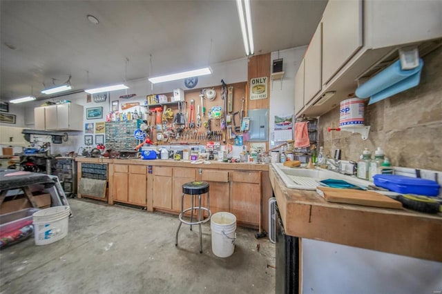 kitchen featuring electric panel, concrete flooring, light countertops, and a sink