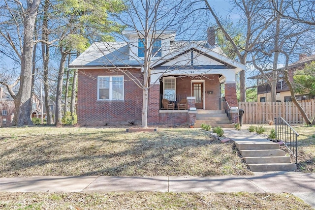 view of front of home featuring fence, covered porch, a chimney, a front lawn, and brick siding