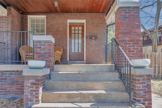 doorway to property featuring brick siding and fence