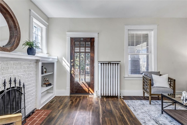 foyer entrance with wood finished floors, visible vents, baseboards, radiator heating unit, and a fireplace