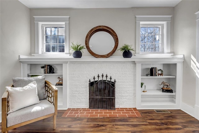 living room with a brick fireplace, wood finished floors, visible vents, and a healthy amount of sunlight