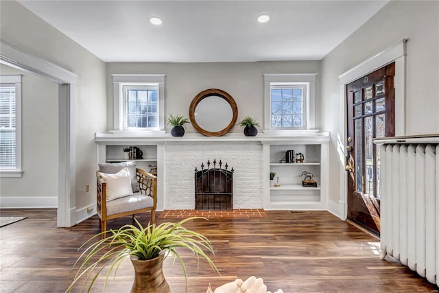 living area featuring radiator, baseboards, recessed lighting, a fireplace, and wood finished floors