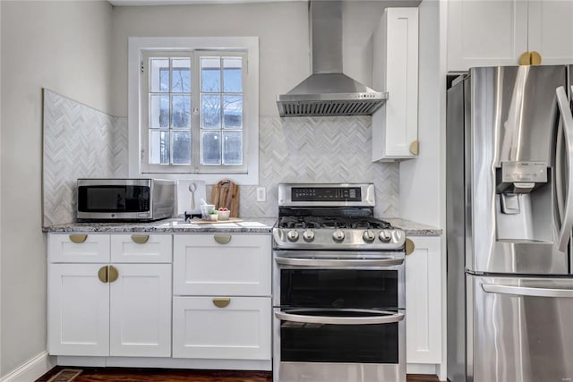 kitchen with backsplash, light stone counters, appliances with stainless steel finishes, white cabinets, and wall chimney exhaust hood