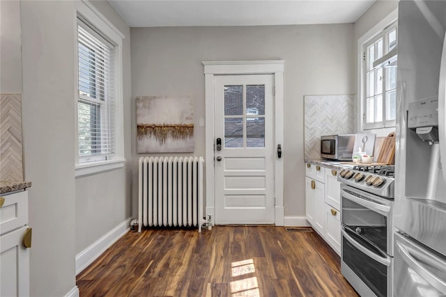 kitchen featuring dark wood-type flooring, tasteful backsplash, radiator heating unit, appliances with stainless steel finishes, and white cabinets