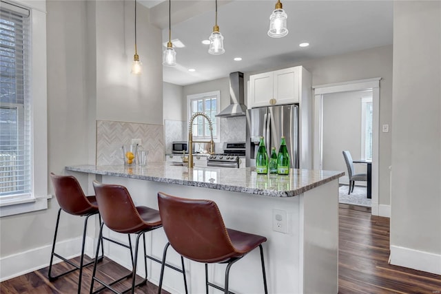 kitchen featuring a breakfast bar, decorative backsplash, dark wood-type flooring, appliances with stainless steel finishes, and wall chimney range hood