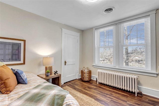 bedroom with visible vents, baseboards, wood finished floors, and radiator heating unit