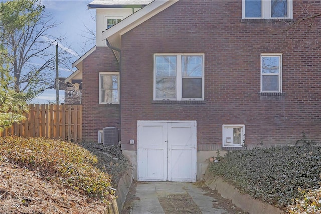 view of property exterior featuring brick siding, central AC unit, and fence