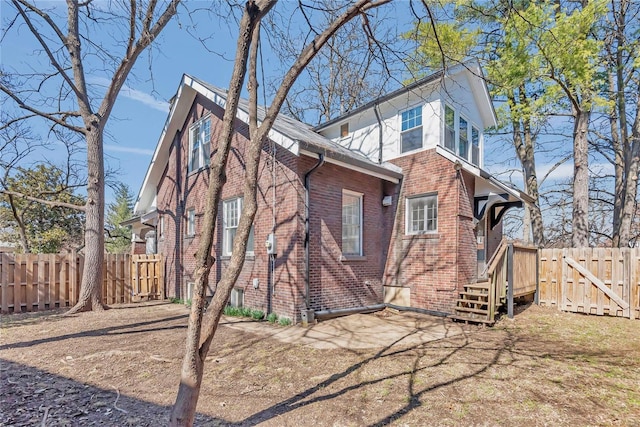 rear view of house featuring a gate, fence, and brick siding