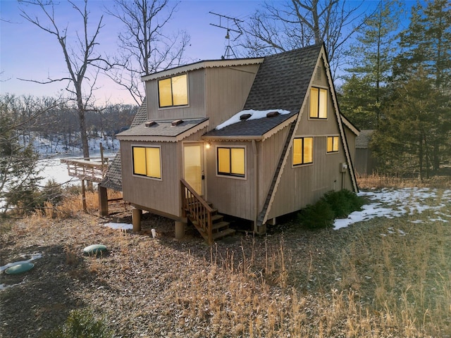 back of house at dusk with roof with shingles