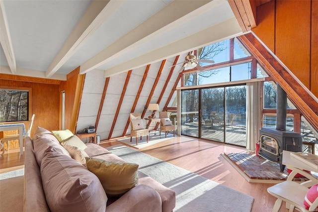 living room with beam ceiling, wood finished floors, wood walls, ceiling fan, and a wood stove