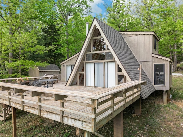 back of property featuring roof with shingles, an outdoor structure, and a deck