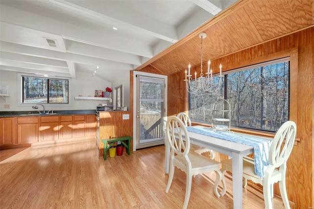 dining area featuring wooden walls, lofted ceiling with beams, light wood-style flooring, and visible vents