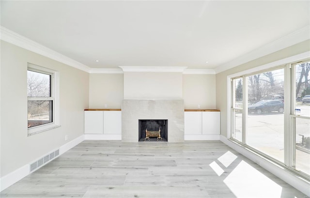 unfurnished living room with visible vents, a healthy amount of sunlight, a tiled fireplace, and crown molding