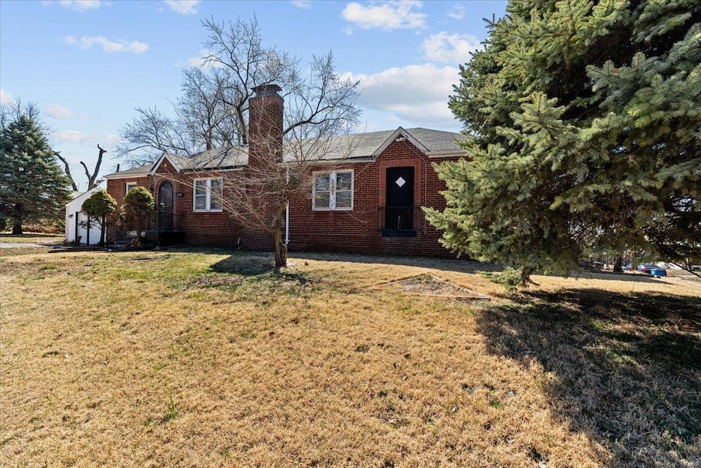 view of front facade featuring brick siding, a chimney, and a front lawn