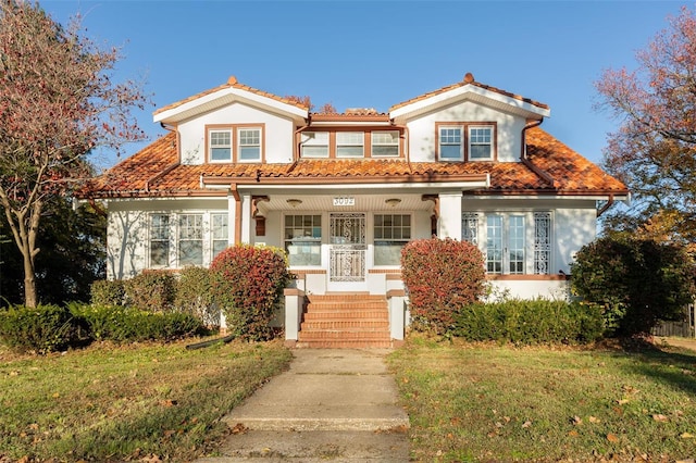 mediterranean / spanish home featuring a porch, stucco siding, a tile roof, and a front lawn