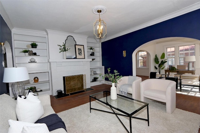 living area featuring built in features, arched walkways, wood finished floors, and ornamental molding