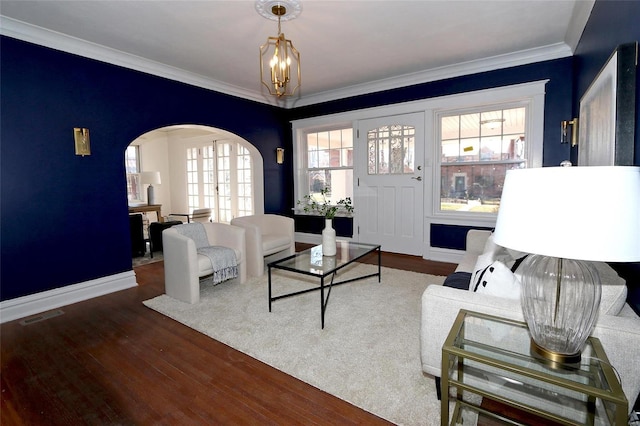 living room with arched walkways, visible vents, crown molding, and wood finished floors