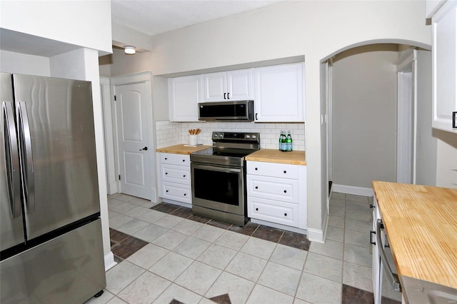 kitchen with arched walkways, stainless steel appliances, wood counters, white cabinetry, and backsplash