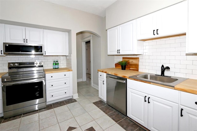 kitchen with a sink, stainless steel appliances, arched walkways, and butcher block countertops