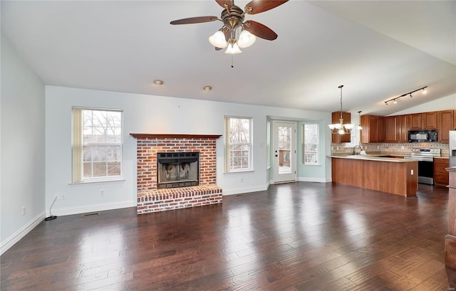 unfurnished living room with lofted ceiling, ceiling fan with notable chandelier, dark wood-style floors, baseboards, and a brick fireplace