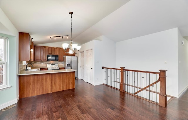 kitchen with a chandelier, vaulted ceiling, appliances with stainless steel finishes, a peninsula, and a sink