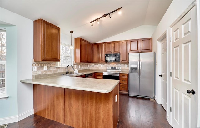 kitchen with brown cabinetry, a peninsula, a sink, vaulted ceiling, and appliances with stainless steel finishes