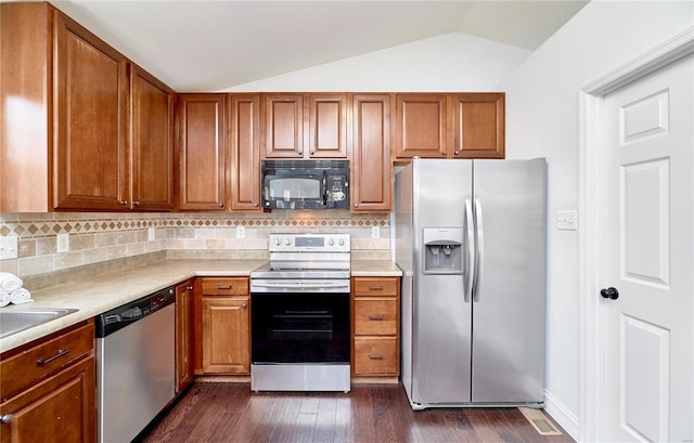 kitchen featuring dark wood-type flooring, stainless steel appliances, brown cabinetry, light countertops, and lofted ceiling