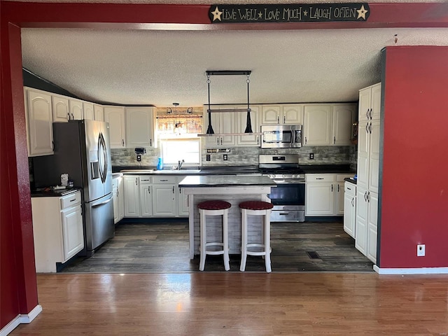 kitchen with dark wood finished floors, a sink, stainless steel appliances, white cabinets, and dark countertops